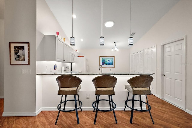 kitchen featuring white cabinets, lofted ceiling, hanging light fixtures, kitchen peninsula, and light hardwood / wood-style flooring