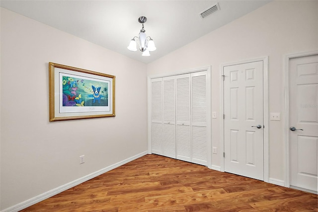 unfurnished bedroom featuring wood-type flooring, lofted ceiling, and a notable chandelier