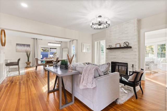 living room featuring hardwood / wood-style flooring, a chandelier, a wealth of natural light, and a stone fireplace