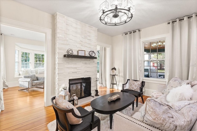 living area featuring an inviting chandelier, hardwood / wood-style floors, and a stone fireplace