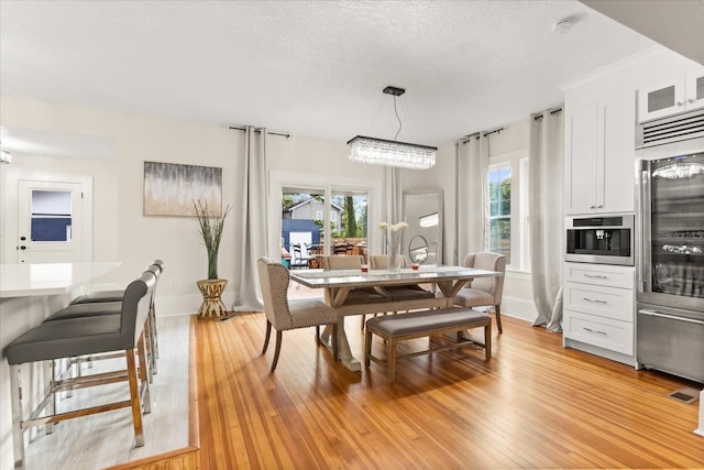 dining area featuring a textured ceiling, a notable chandelier, and light hardwood / wood-style flooring