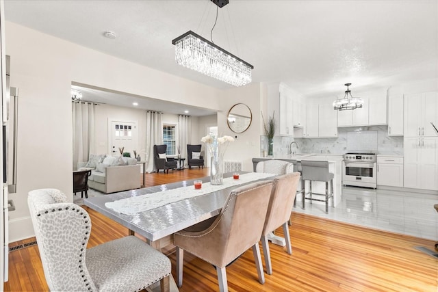 dining space with sink, a notable chandelier, and light wood-type flooring