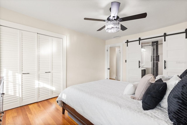 bedroom featuring connected bathroom, ceiling fan, hardwood / wood-style flooring, a closet, and a barn door