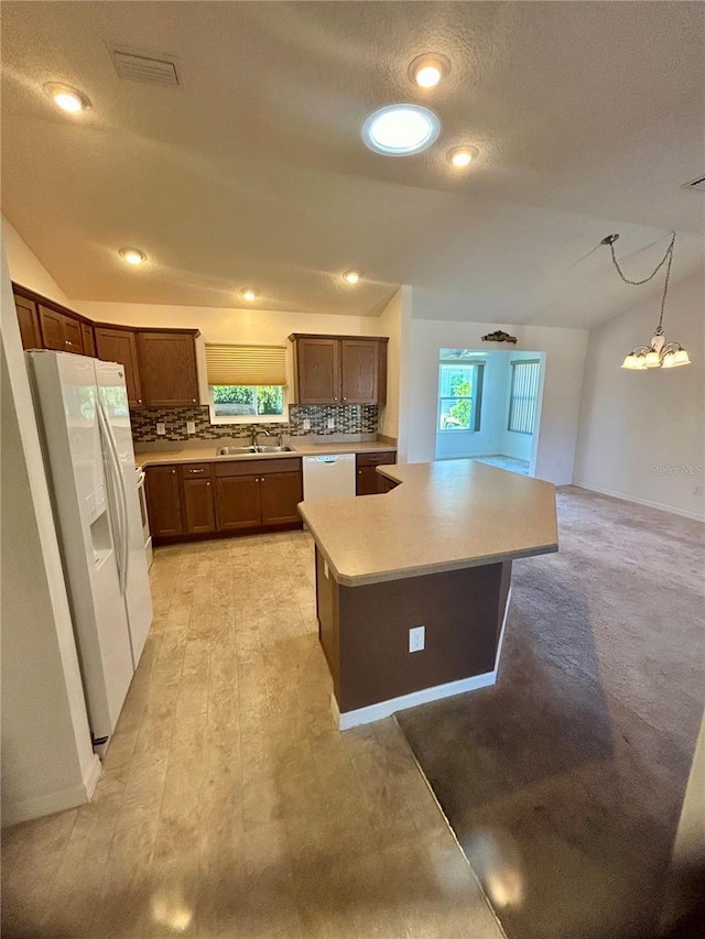 kitchen featuring white appliances, a kitchen island, decorative light fixtures, sink, and vaulted ceiling