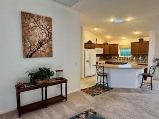 kitchen with a breakfast bar, white appliances, brown cabinetry, light countertops, and vaulted ceiling