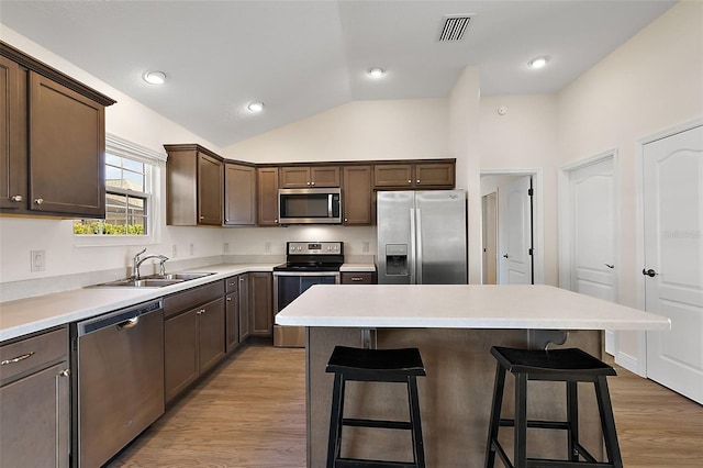 kitchen with a kitchen island, stainless steel appliances, sink, vaulted ceiling, and light hardwood / wood-style flooring