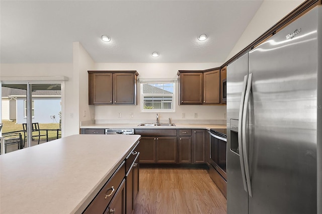 kitchen with light hardwood / wood-style floors, appliances with stainless steel finishes, lofted ceiling, dark brown cabinets, and sink