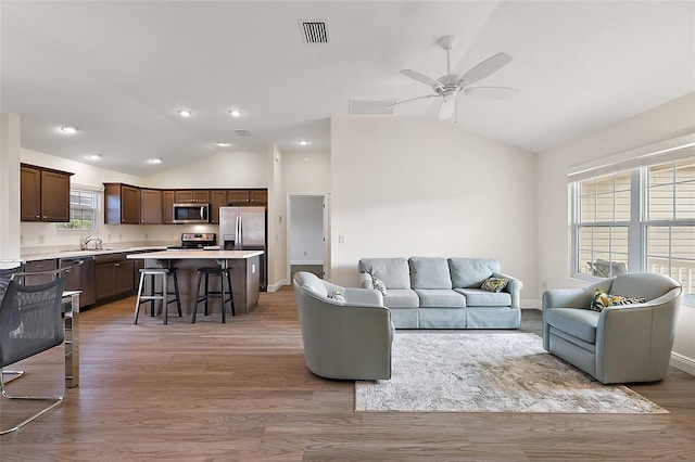 living room featuring light wood-type flooring, vaulted ceiling, sink, and ceiling fan