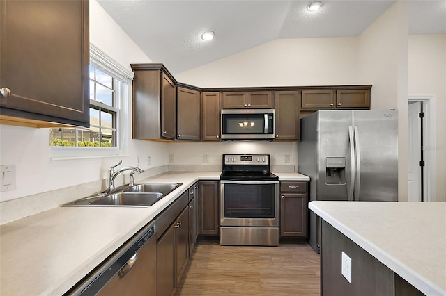 kitchen with vaulted ceiling, light hardwood / wood-style flooring, sink, stainless steel appliances, and dark brown cabinets