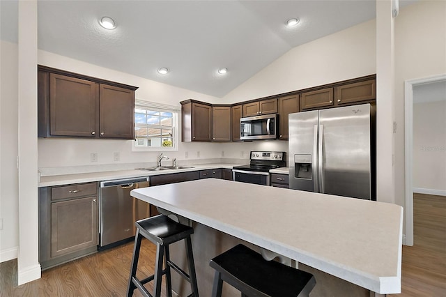 kitchen featuring stainless steel appliances, vaulted ceiling, a breakfast bar, a kitchen island, and sink