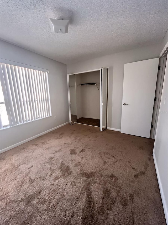 unfurnished bedroom with dark carpet, a textured ceiling, and a closet