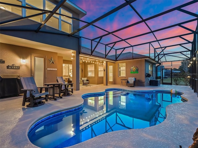 pool at dusk featuring glass enclosure and a patio