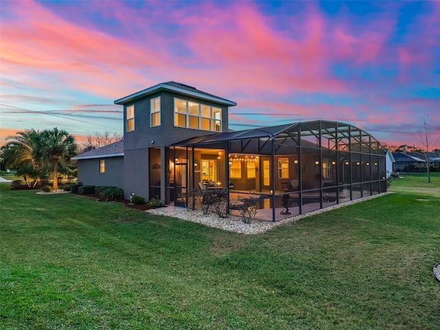 back house at dusk with a lawn, a patio, and glass enclosure