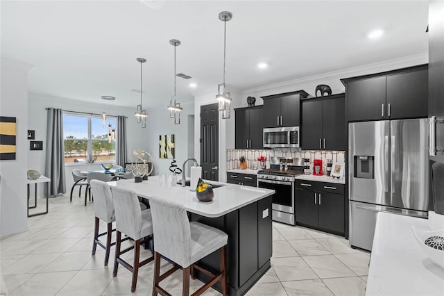 kitchen featuring a breakfast bar, sink, decorative light fixtures, stainless steel appliances, and a kitchen island with sink