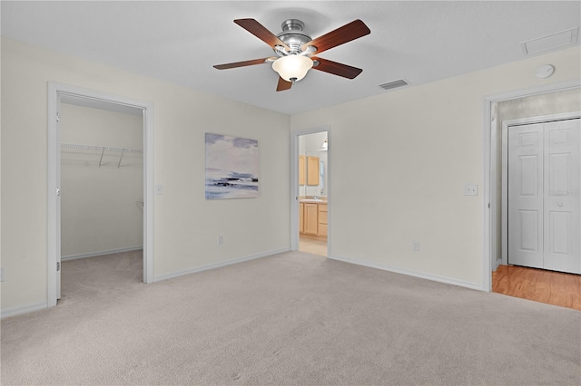 unfurnished bedroom featuring light carpet, a spacious closet, a closet, and ceiling fan