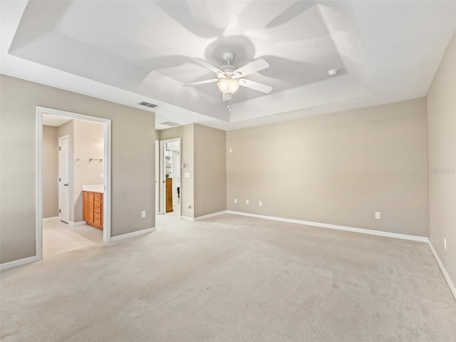 unfurnished bedroom with ceiling fan, light colored carpet, connected bathroom, and a tray ceiling