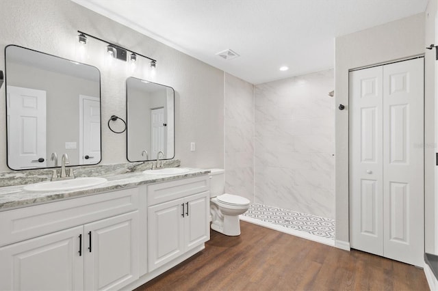 bathroom featuring hardwood / wood-style floors, toilet, vanity, and a tile shower