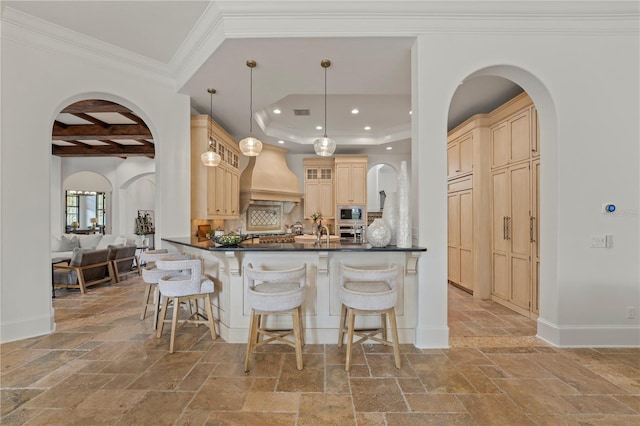 kitchen with kitchen peninsula, built in microwave, hanging light fixtures, custom range hood, and coffered ceiling