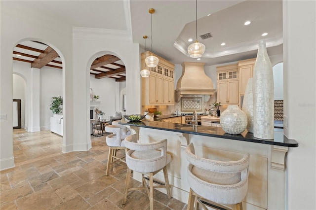 kitchen with backsplash, beamed ceiling, custom range hood, decorative light fixtures, and kitchen peninsula