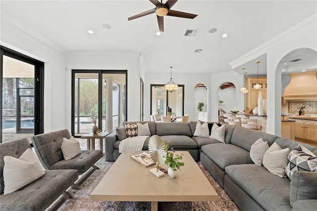 living room with ceiling fan with notable chandelier and crown molding