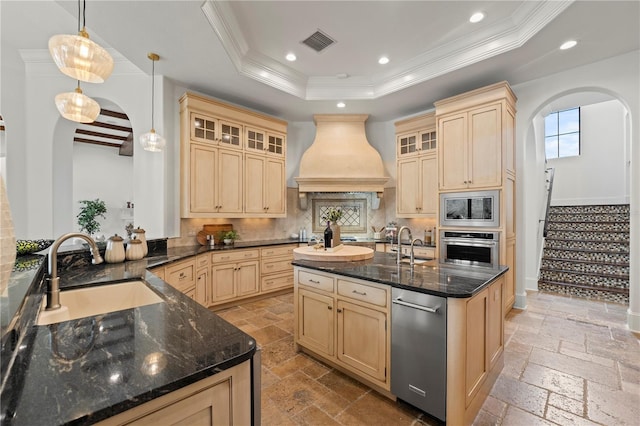 kitchen featuring appliances with stainless steel finishes, custom range hood, pendant lighting, a raised ceiling, and sink