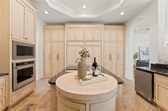 kitchen with built in microwave, light brown cabinetry, stainless steel oven, a tray ceiling, and ornamental molding