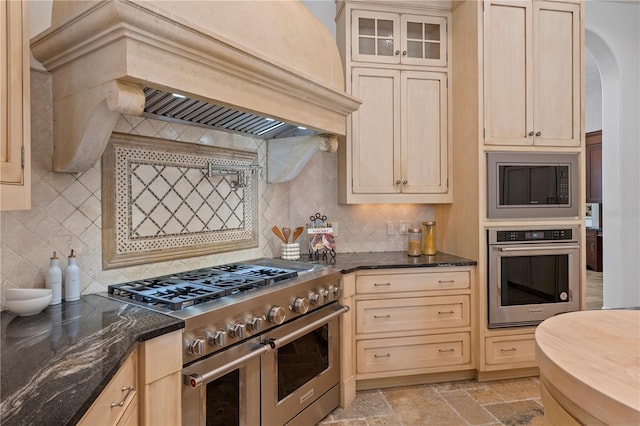 kitchen featuring dark stone counters, custom exhaust hood, stainless steel appliances, and decorative backsplash