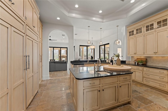 kitchen featuring sink, decorative light fixtures, a raised ceiling, an island with sink, and ornamental molding