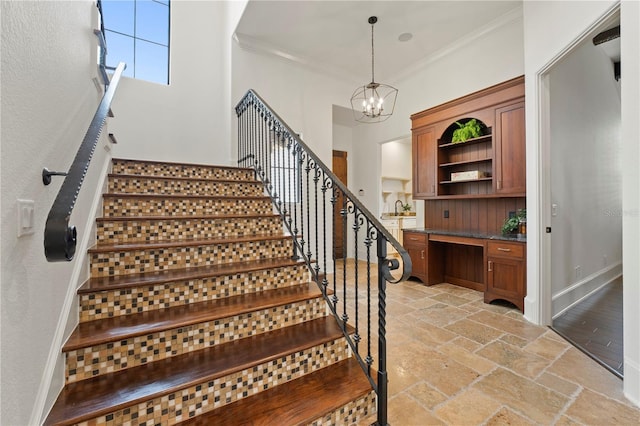 staircase featuring a high ceiling, built in desk, a chandelier, ornamental molding, and sink