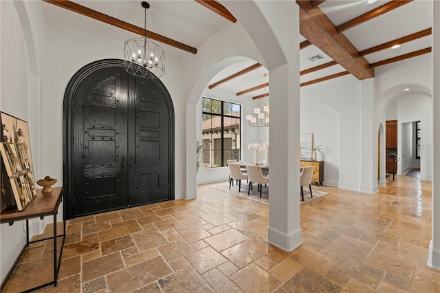 entrance foyer featuring a chandelier, a towering ceiling, and beam ceiling