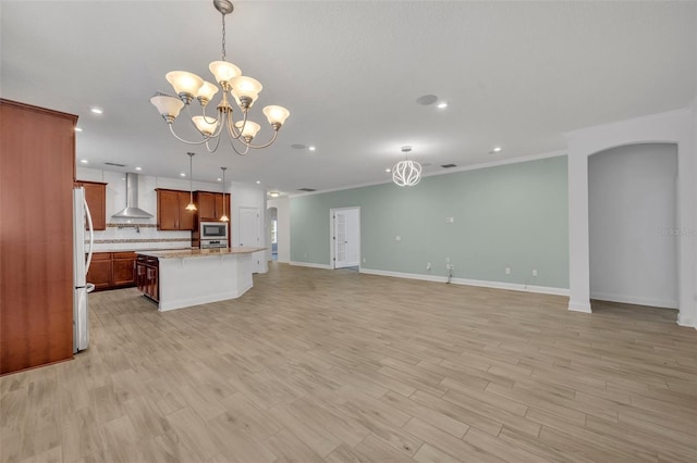 kitchen with pendant lighting, wall chimney range hood, a kitchen island with sink, and built in microwave