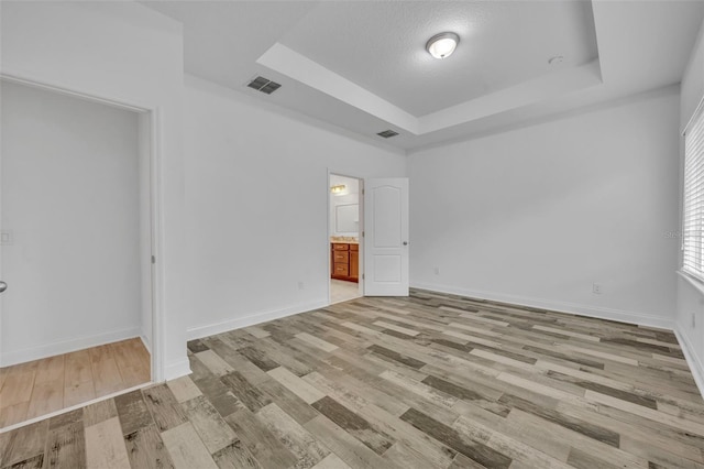 unfurnished room featuring a raised ceiling, light wood-type flooring, and a textured ceiling