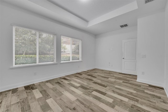 unfurnished room with a raised ceiling, a textured ceiling, and light wood-type flooring