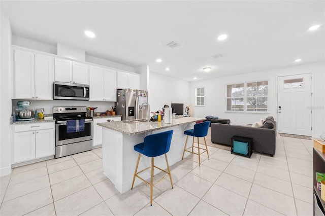 kitchen with white cabinetry, light stone counters, an island with sink, and appliances with stainless steel finishes