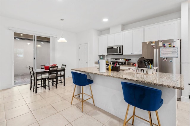 kitchen featuring appliances with stainless steel finishes, white cabinetry, hanging light fixtures, a kitchen island with sink, and a kitchen bar