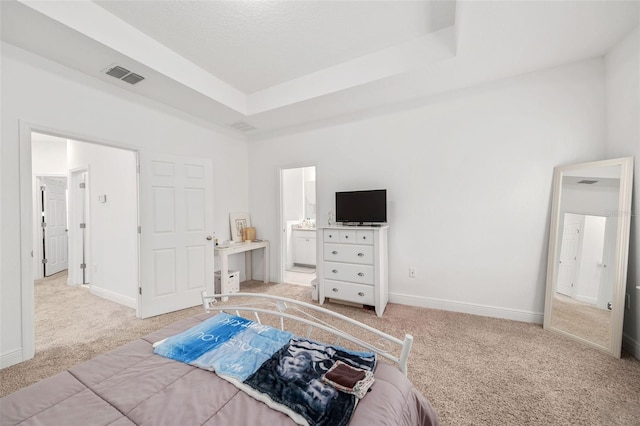 bedroom featuring light carpet, connected bathroom, and a tray ceiling