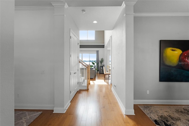 corridor featuring crown molding, light hardwood / wood-style flooring, and ornate columns