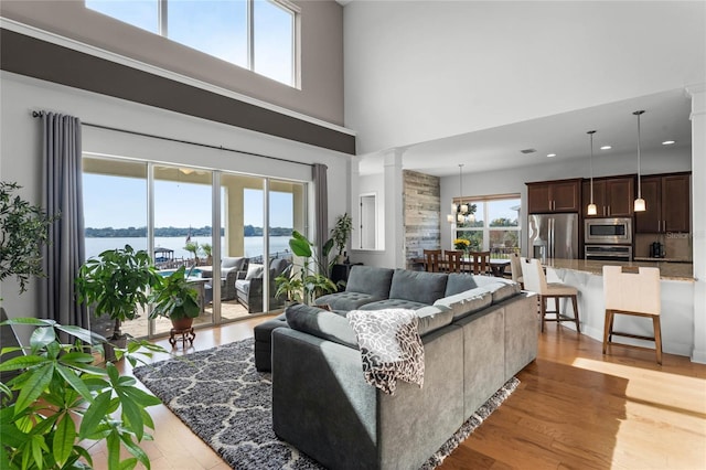 living room with a water view, light wood-type flooring, and ornate columns