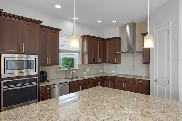 kitchen with sink, hanging light fixtures, stainless steel appliances, light stone counters, and wall chimney exhaust hood