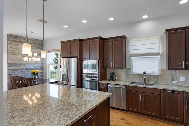 kitchen featuring sink, light stone counters, tasteful backsplash, decorative light fixtures, and stainless steel appliances