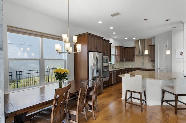 kitchen featuring pendant lighting, wall chimney range hood, sink, and appliances with stainless steel finishes