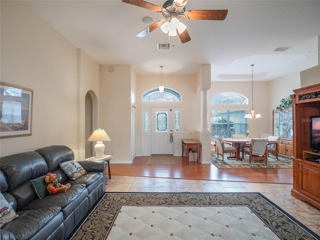 tiled foyer entrance with ornate columns, ceiling fan with notable chandelier, and a tray ceiling