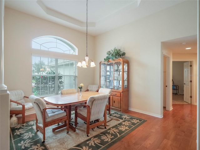 dining space with a raised ceiling, wood-type flooring, and an inviting chandelier