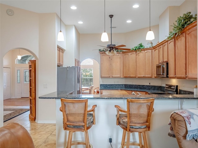 27504 Stoney Brook Dr, Leesburg, FL 34748 - kitchen featuring stainless steel appliances, arched walkways, a ceiling fan, a peninsula, and dark stone counters