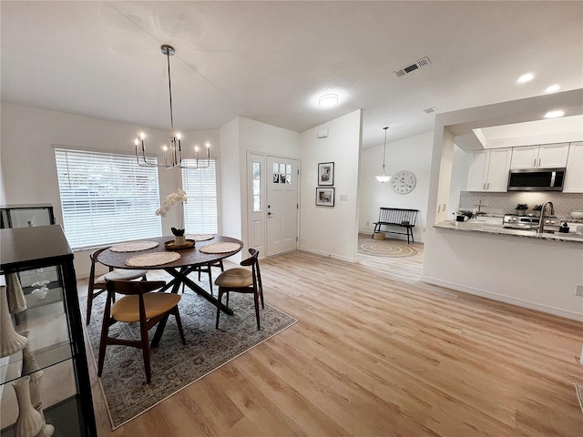 dining room with sink, light hardwood / wood-style flooring, a notable chandelier, and vaulted ceiling