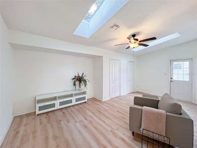 living room with ceiling fan, vaulted ceiling with skylight, a textured ceiling, and light wood-type flooring