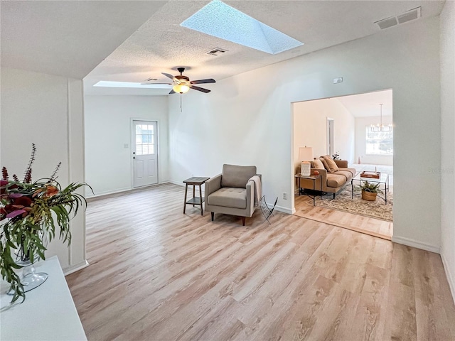 living area with light wood-type flooring, a skylight, a textured ceiling, and ceiling fan with notable chandelier