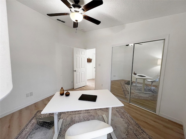 home office featuring a textured ceiling, ceiling fan, and light hardwood / wood-style floors