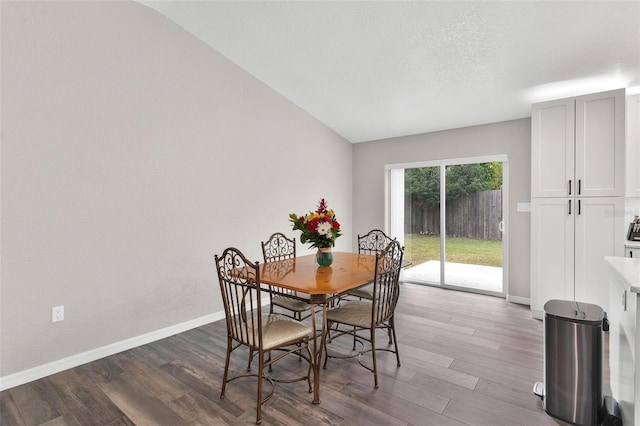 dining space featuring vaulted ceiling and dark wood-type flooring