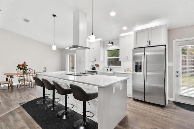 kitchen with white cabinetry, extractor fan, stainless steel fridge, pendant lighting, and a center island